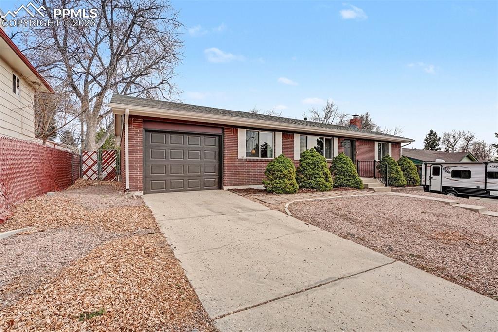 Single story home featuring brick siding, concrete driveway, a garage, a chimney, and roof with shingles