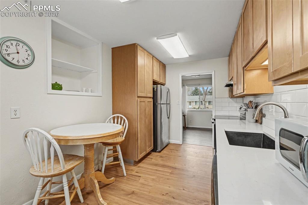 Kitchen with stainless steel appliances, light wood-style flooring, light stone counters, and decorative backsplash