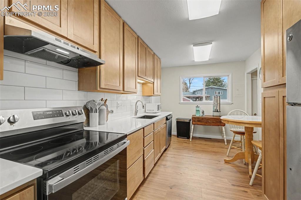 Kitchen featuring stainless steel appliances, light wood-type flooring, backsplash, light stone counters, and wood finish cabinets