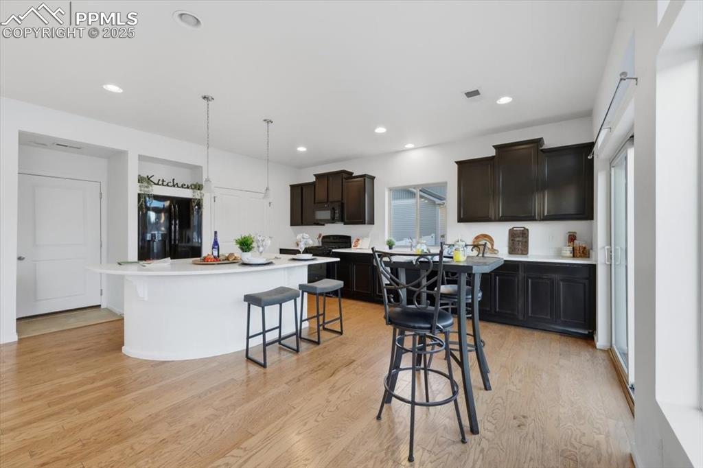 Kitchen featuring light wood-type flooring, black appliances, a breakfast bar, pendant lighting, and a center island