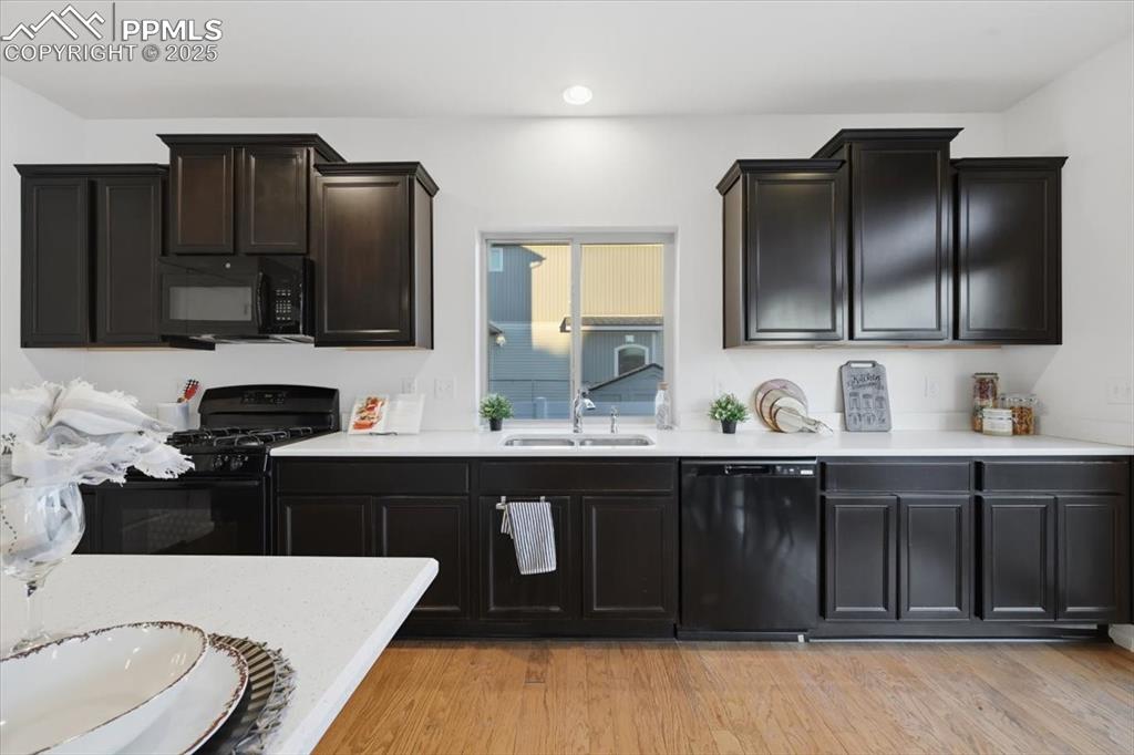 Kitchen featuring black appliances, light wood-style floors, light stone countertops, recessed lighting, and dark cabinets