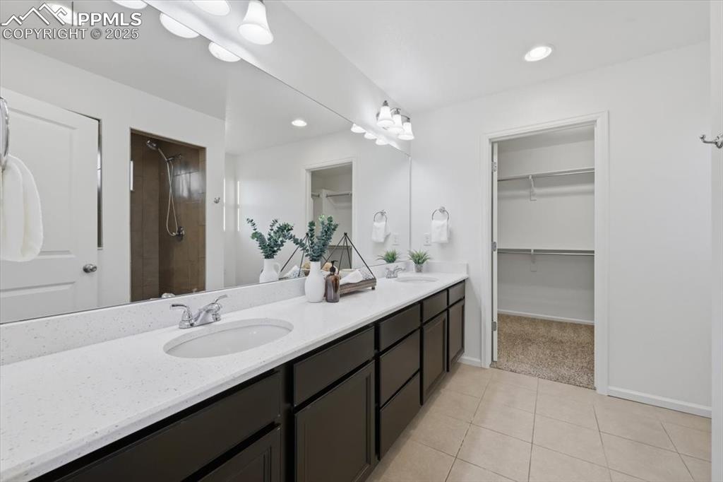 Bathroom featuring double vanity, light tile patterned flooring, tiled shower, a walk in closet, and recessed lighting