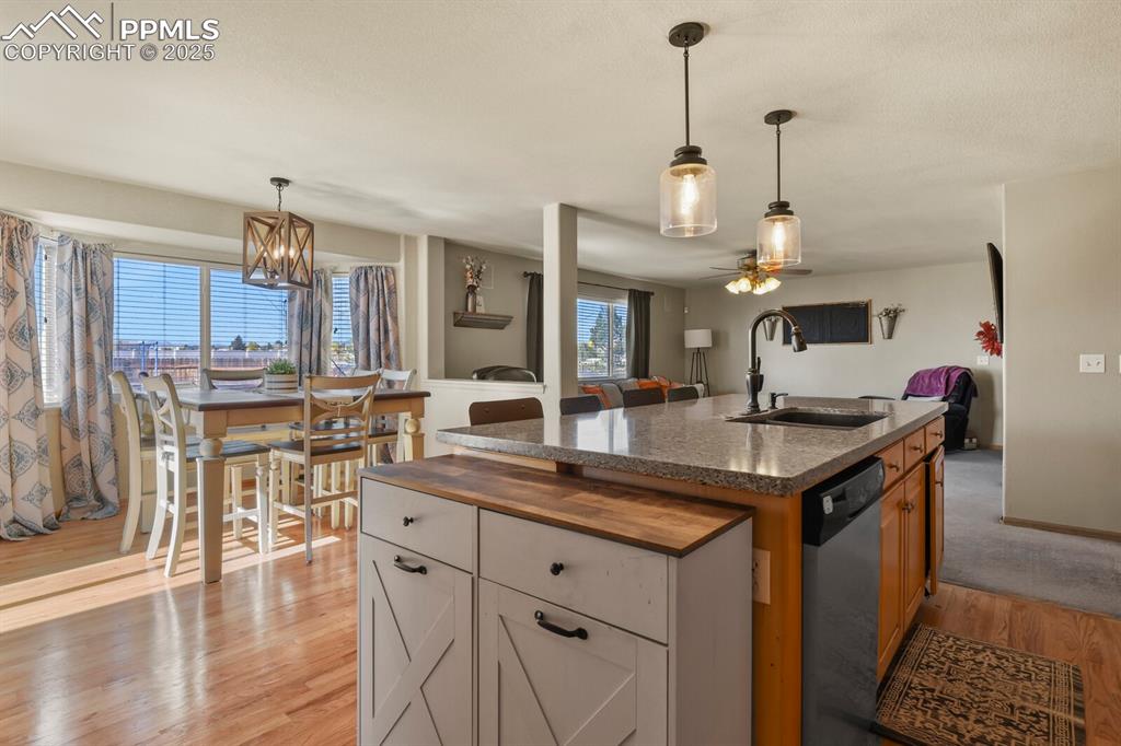 Kitchen with hanging light fixtures, wood counters, an island with sink, and dishwasher