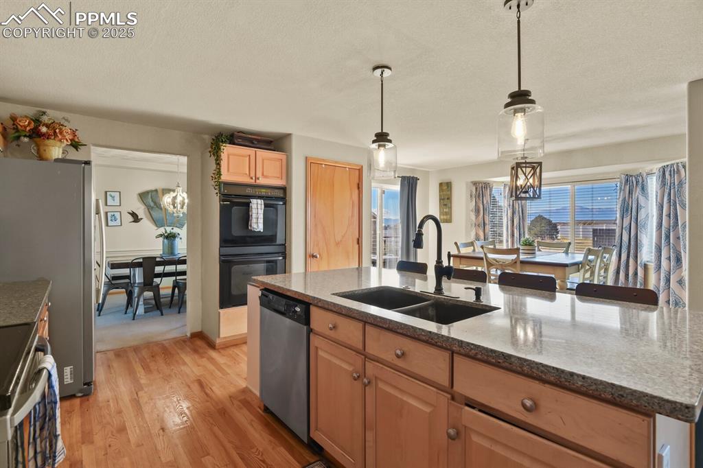 Kitchen featuring a chandelier, hanging light fixtures, light wood finished floors, stainless steel appliances, and a center island with sink