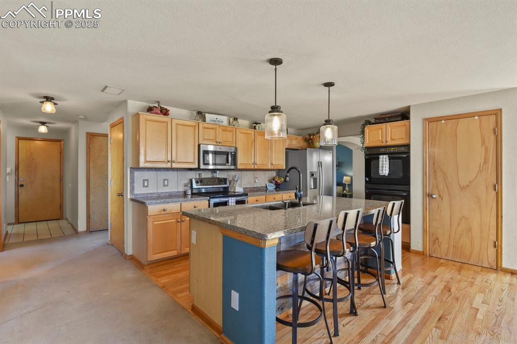 Kitchen with stainless steel appliances, an island with sink, a breakfast bar, hanging light fixtures, and decorative backsplash