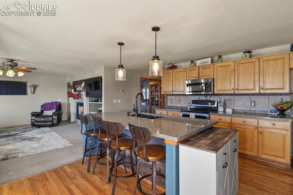 Kitchen featuring tasteful backsplash, a breakfast bar, stainless steel appliances, hanging light fixtures, and a glass covered fireplace