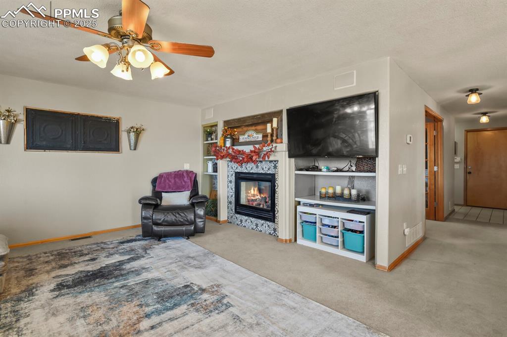 Living area featuring light colored carpet, a fireplace, built in features, a ceiling fan, and a textured ceiling