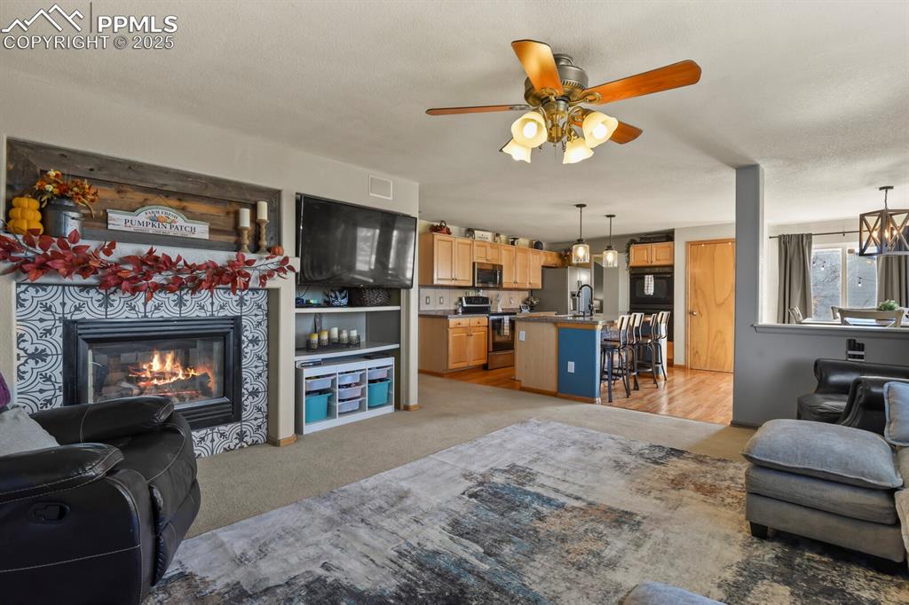 Living area with light colored carpet, a tile fireplace, and ceiling fan
