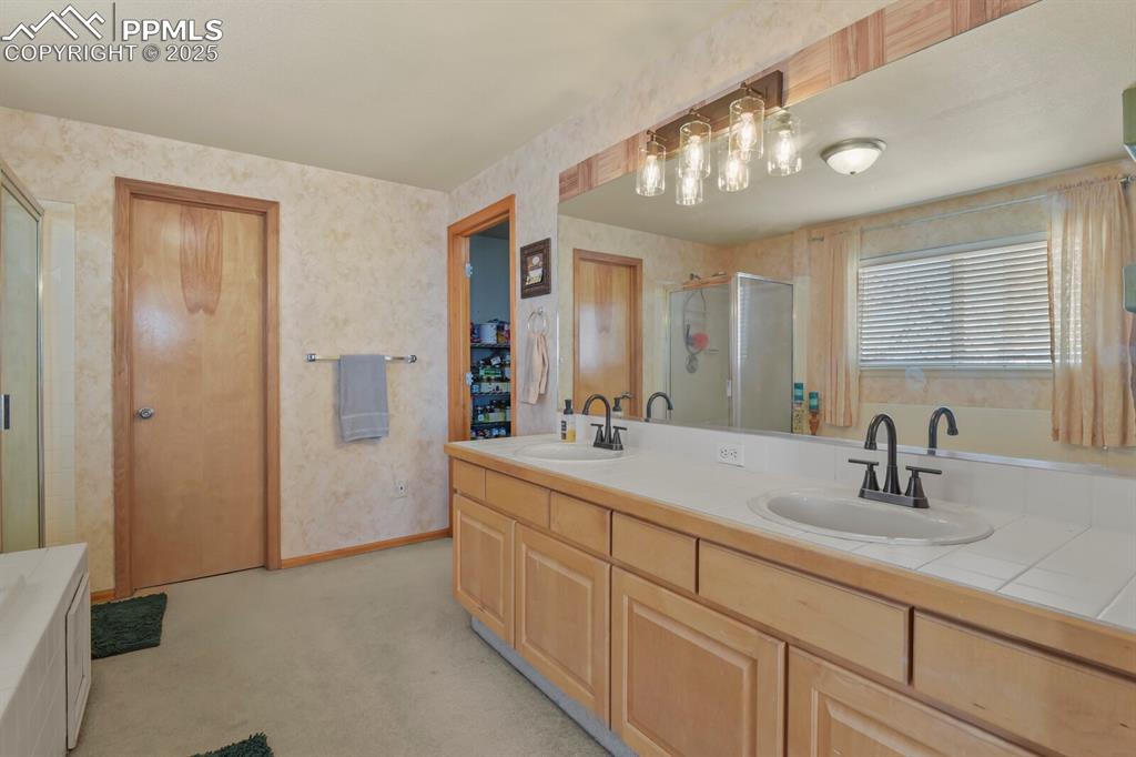 Bathroom featuring double vanity, wallpapered walls, a stall shower, a tub, and light carpet