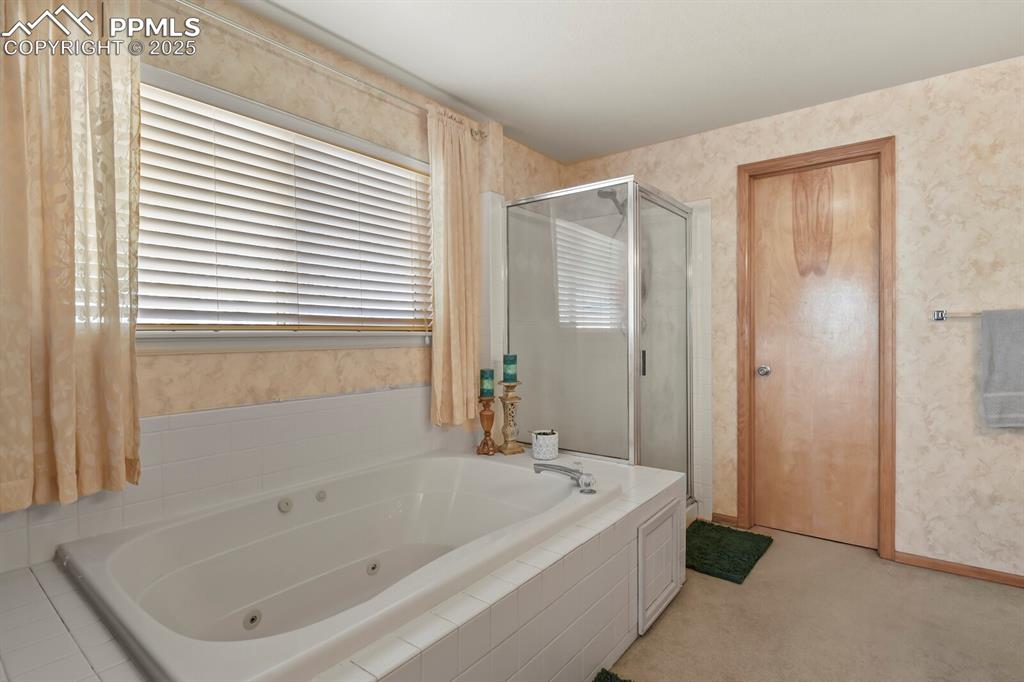 Full bathroom featuring wallpapered walls, a tub with jets, a stall shower, and light carpet