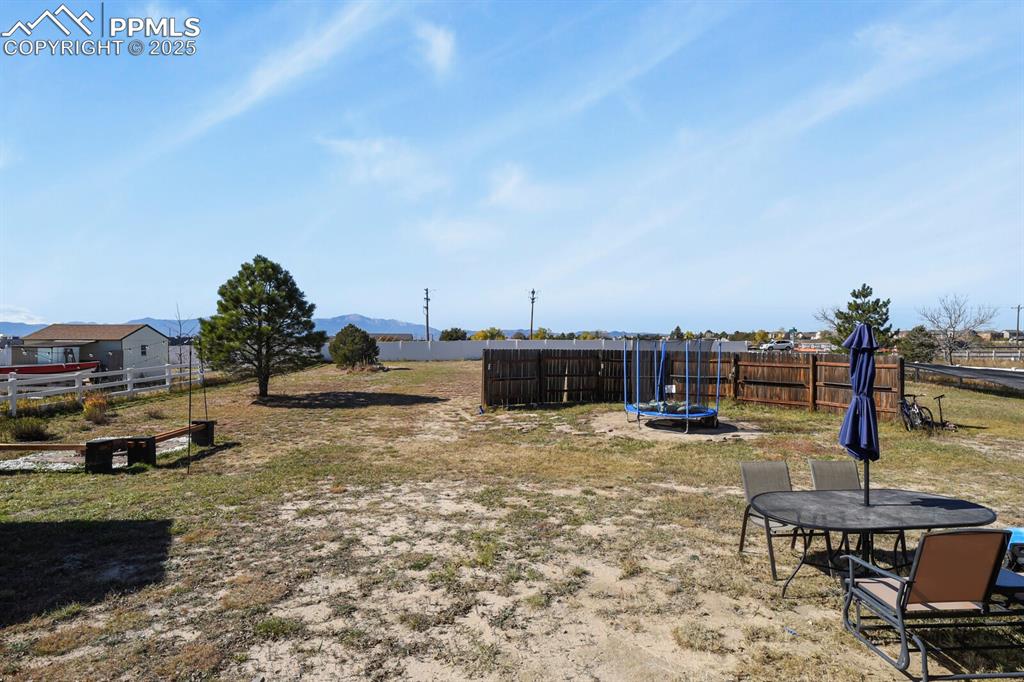 Fenced backyard featuring a trampoline, a mountain view, and a patio