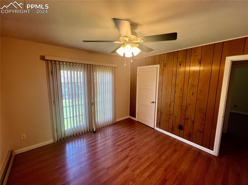 Unfurnished bedroom featuring ceiling fan, wooden walls, baseboard heating, and dark hardwood / wood-style floors