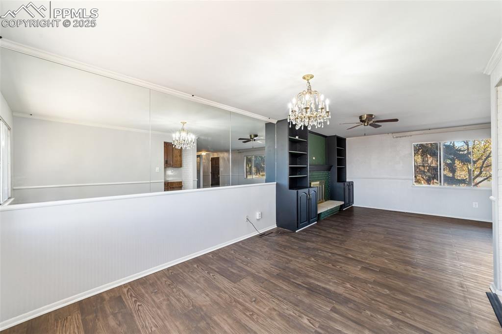 Empty room featuring a chandelier, ceiling fan, dark wood-type flooring, and crown molding