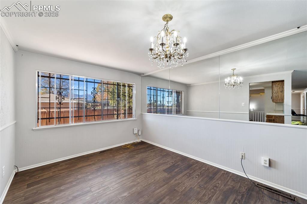 Unfurnished dining area with dark wood-type flooring, a chandelier, and crown molding