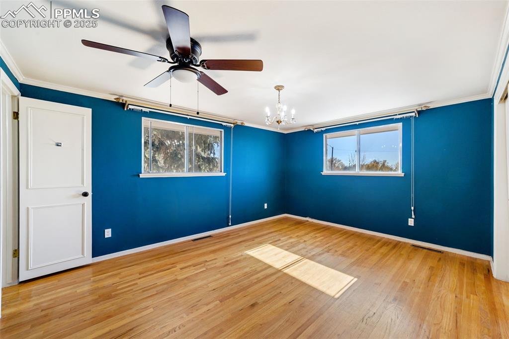 Empty room with a chandelier, light wood-style flooring, ornamental molding, plenty of natural light, and a ceiling fan