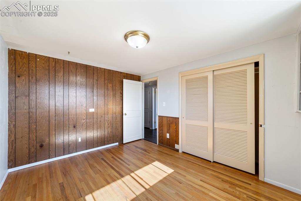 Unfurnished bedroom featuring wooden walls, light wood-style flooring, and a closet