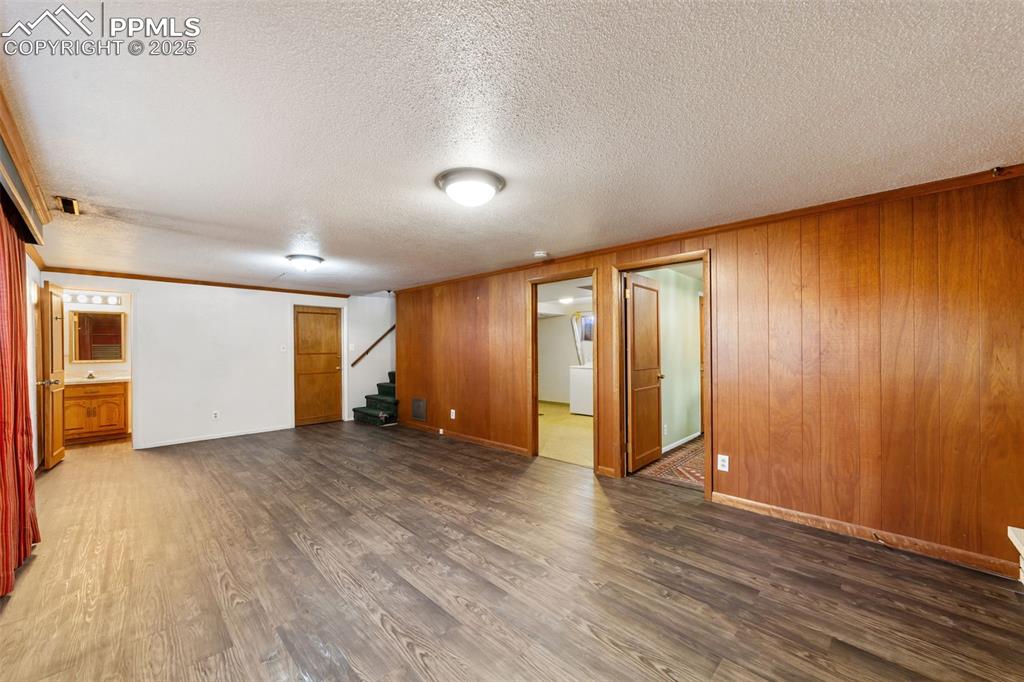 Unfurnished room with ornamental molding, stairway, dark wood finished floors, wooden walls, and a textured ceiling