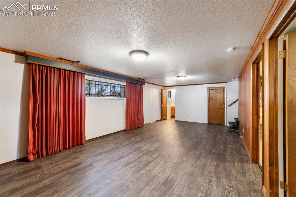 Spare room with dark wood-style flooring, a textured ceiling, crown molding, and stairway