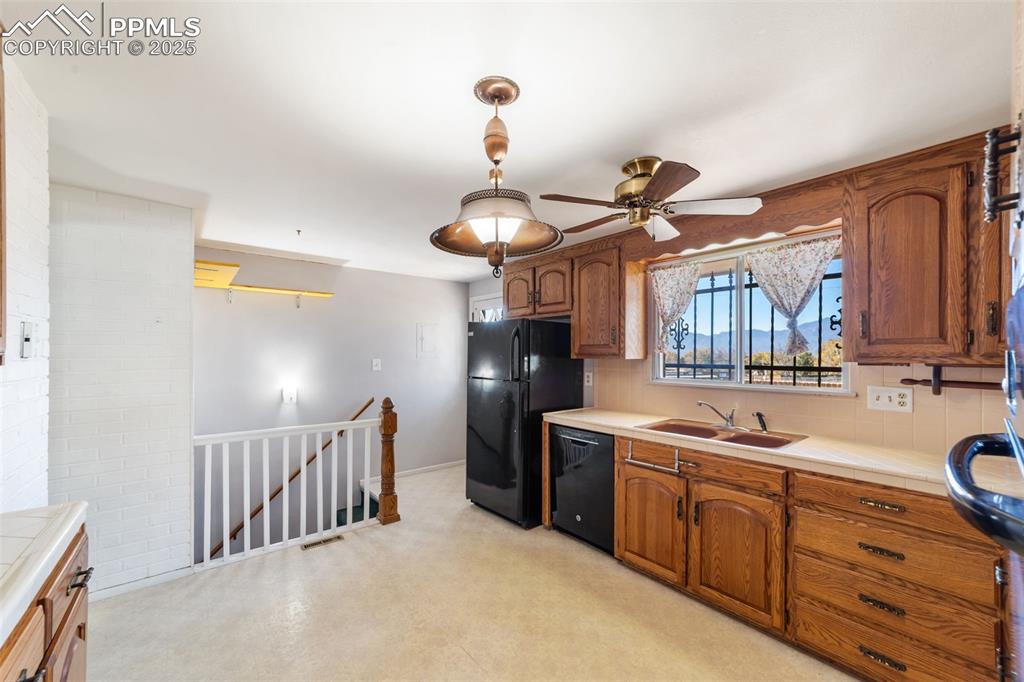 Kitchen featuring brown cabinets, backsplash, tile counters, black dishwasher, and ceiling fan