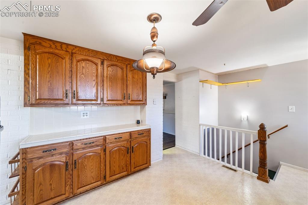 Kitchen with backsplash, decorative light fixtures, brown cabinetry, tile counters, and light floors