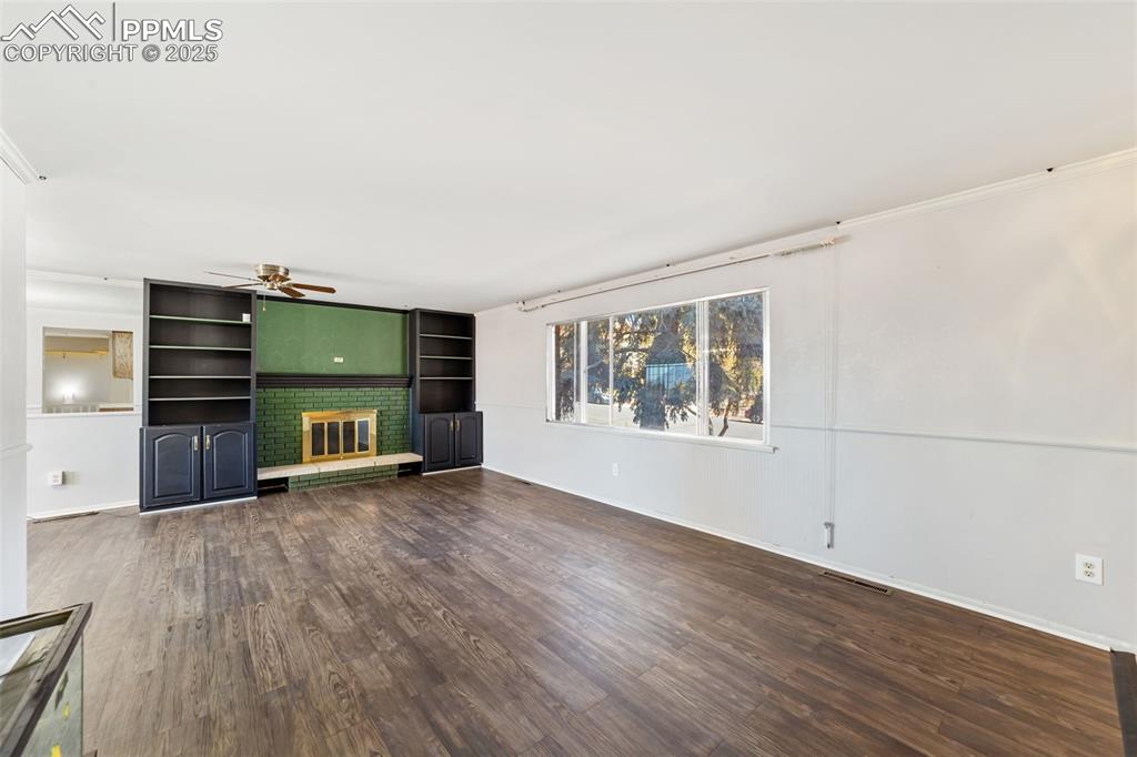 Unfurnished living room featuring dark wood-type flooring, a brick fireplace, and ceiling fan