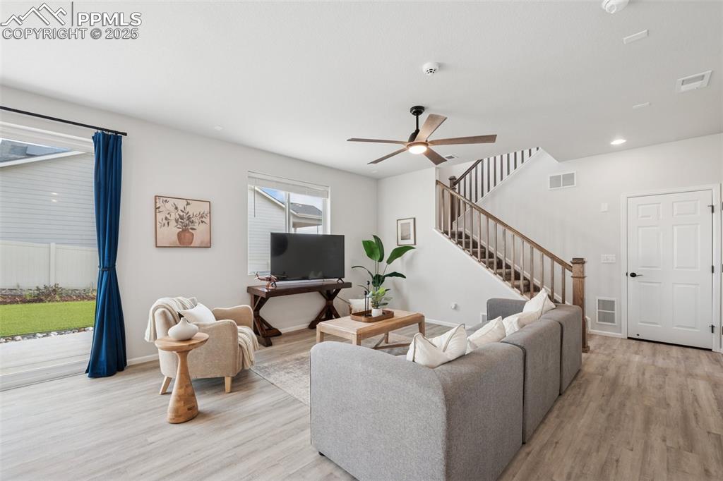 Living area featuring light wood-style floors, ceiling fan, stairway, and recessed lighting