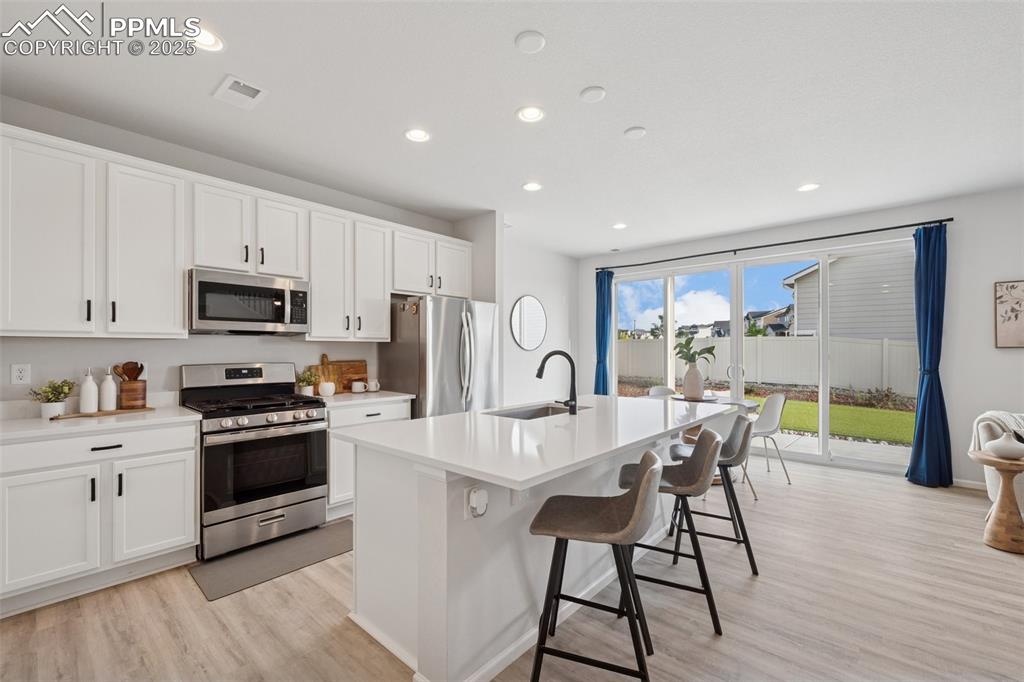 Kitchen with appliances with stainless steel finishes, light wood-style flooring, recessed lighting, a kitchen bar, and a center island with sink