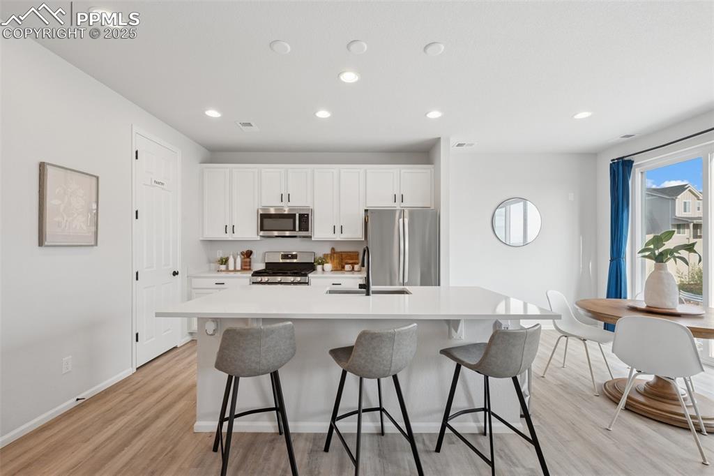 Kitchen with a center island with sink, appliances with stainless steel finishes, light wood-style floors, light countertops, and recessed lighting
