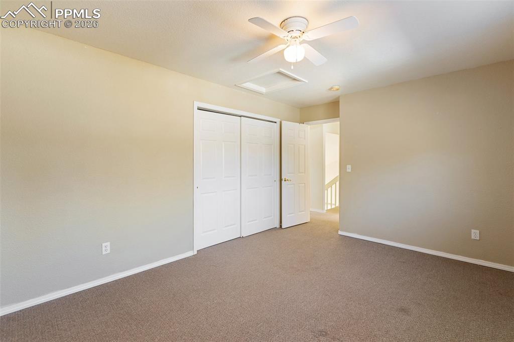 Unfurnished bedroom with attic access, carpet, a ceiling fan, and a closet