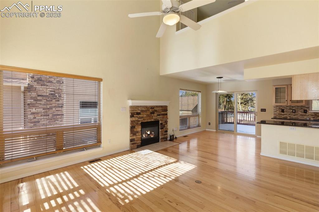 Unfurnished living room with a fireplace, light wood-style floors, ceiling fan, and a high ceiling