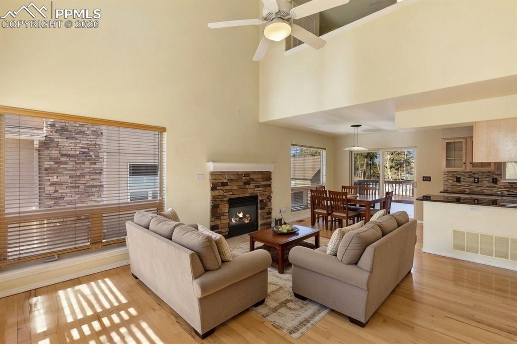 Living area with light wood finished floors, a fireplace, a ceiling fan, and a high ceiling