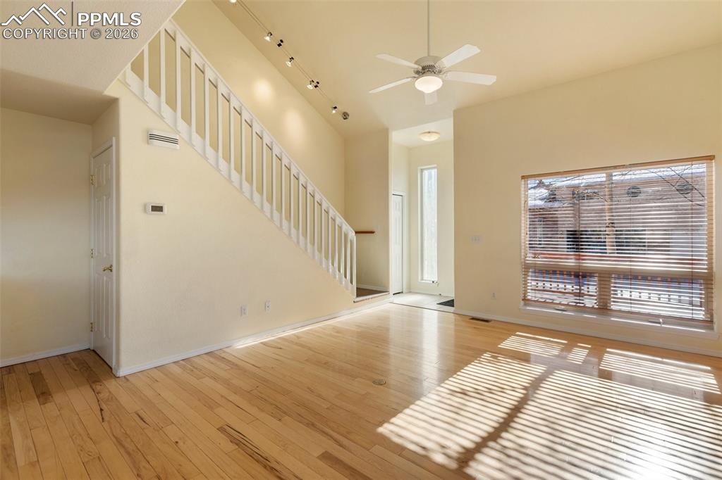 Unfurnished living room with a towering ceiling, light wood-style floors, stairs, and a ceiling fan