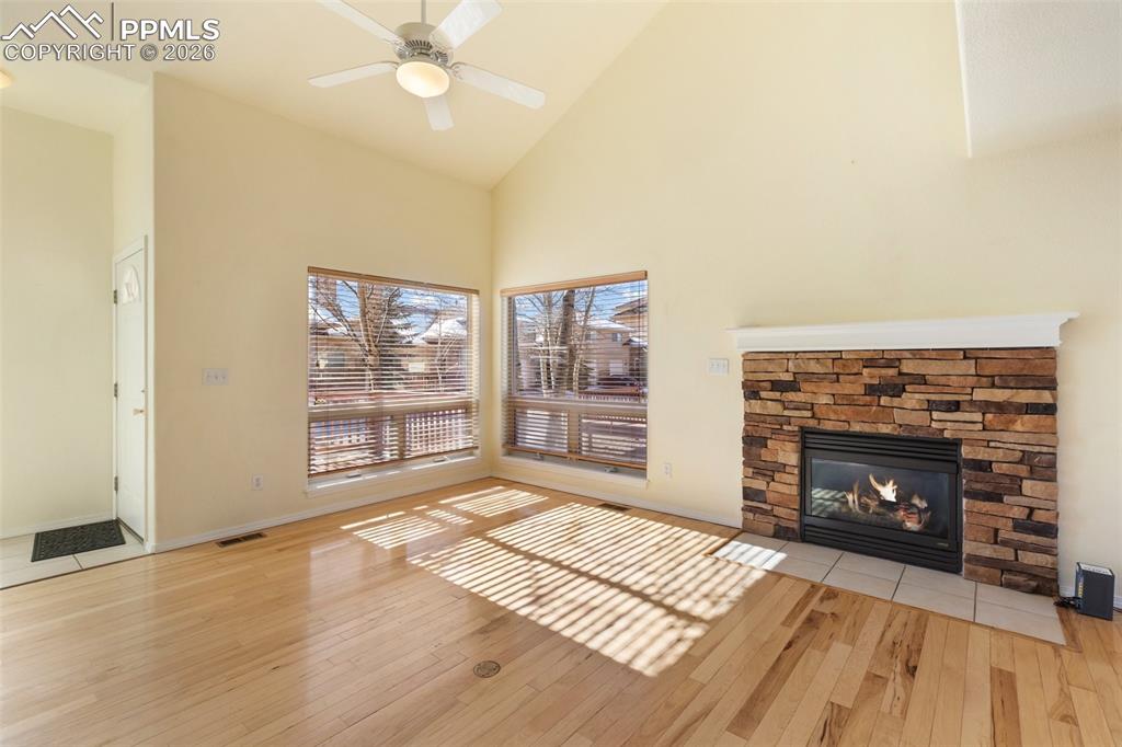 Unfurnished living room with light wood-style floors, high vaulted ceiling, a fireplace, and a ceiling fan