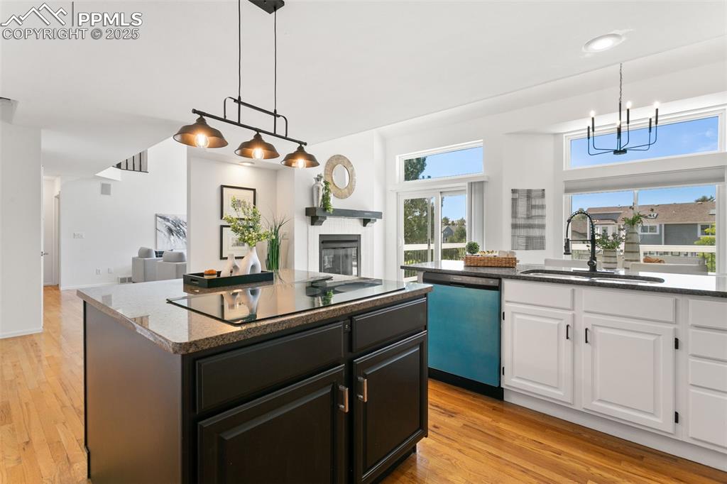 Kitchen featuring light wood-type flooring, a glass covered fireplace, white cabinetry, open floor plan, and dishwashing machine