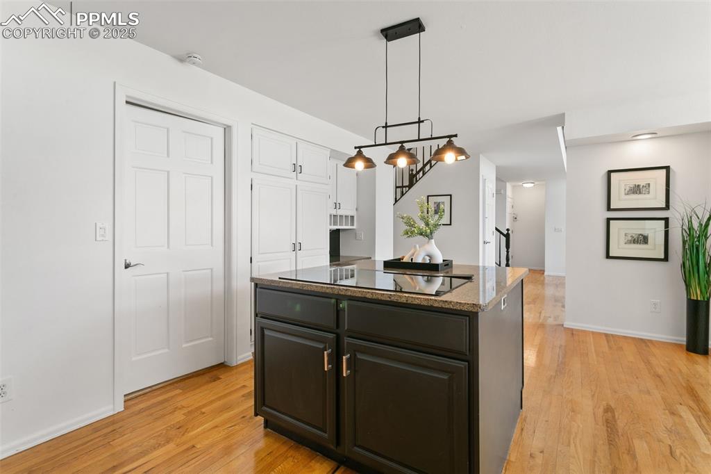 Kitchen featuring light wood-style floors, a center island, dark stone countertops, and pendant lighting