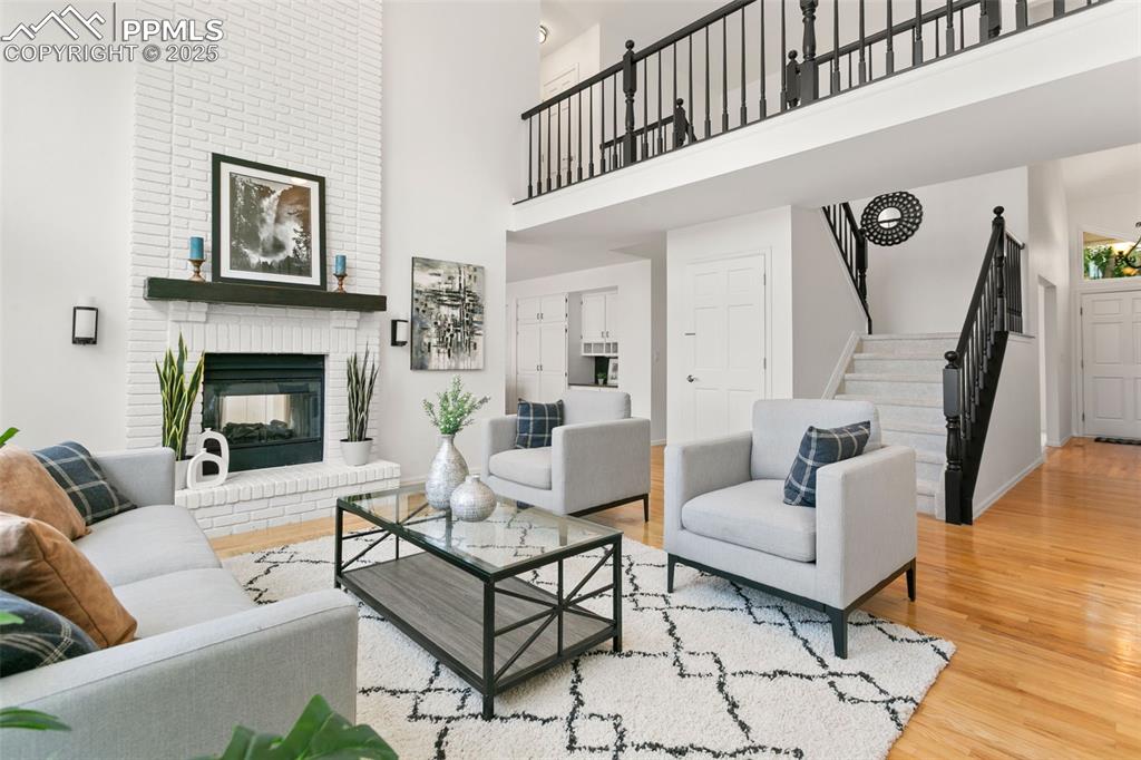 Living area featuring wood finished floors, a high ceiling, stairs, and a brick fireplace