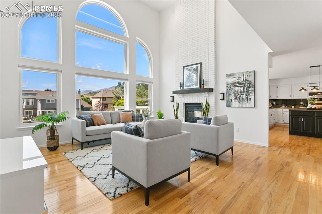Living area featuring a brick fireplace, light wood-type flooring, plenty of natural light, and a high ceiling