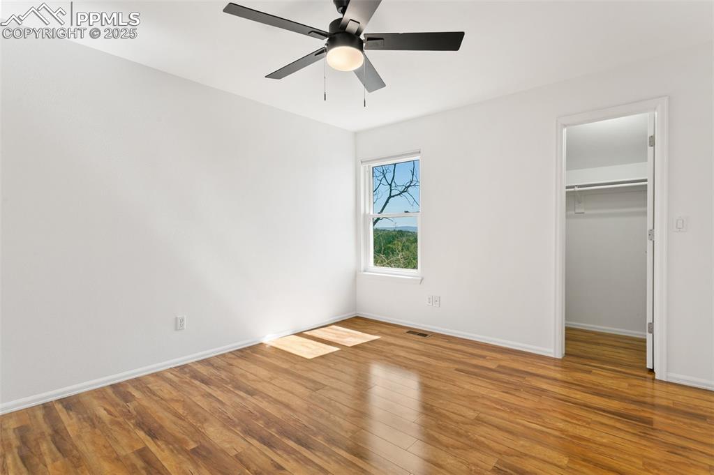 Unfurnished bedroom with wood finished floors, a walk in closet, and ceiling fan