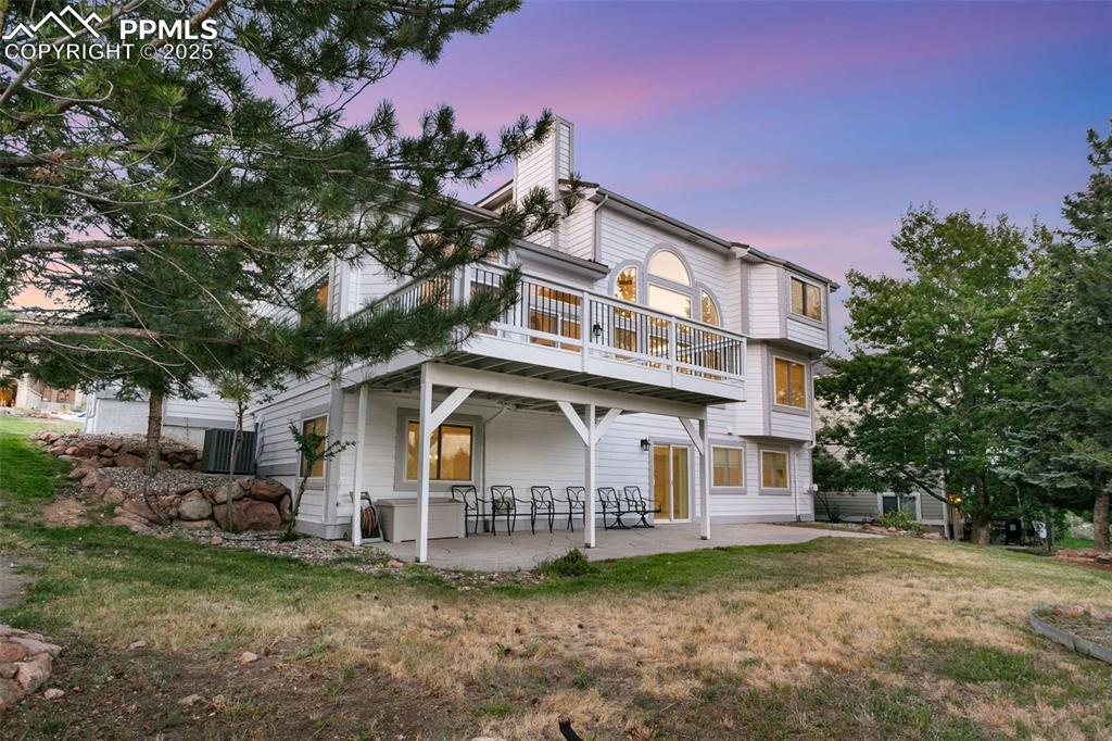 View of front of house with a patio area, a chimney, a lawn, and a balcony
