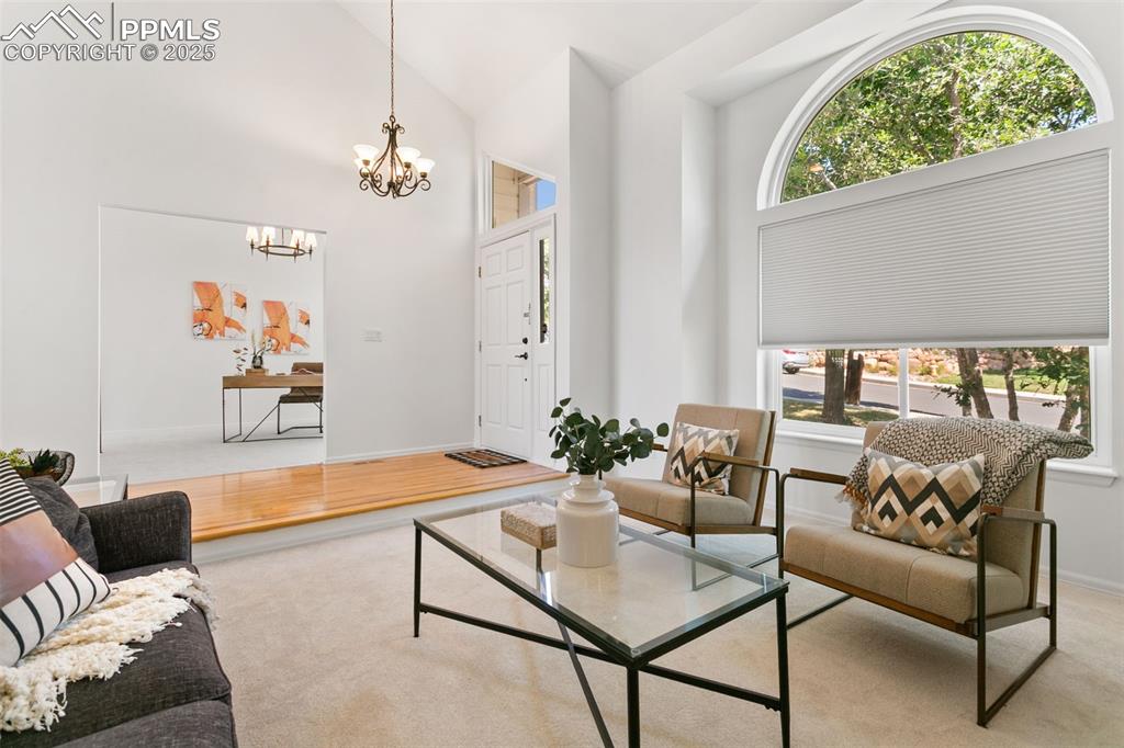 Living room with light carpet, a chandelier, light wood-type flooring, and high vaulted ceiling