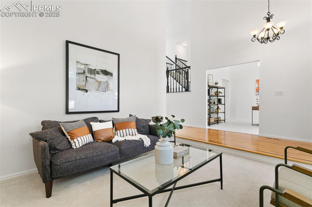 Living room featuring a high ceiling, stairs, a chandelier, and carpet floors