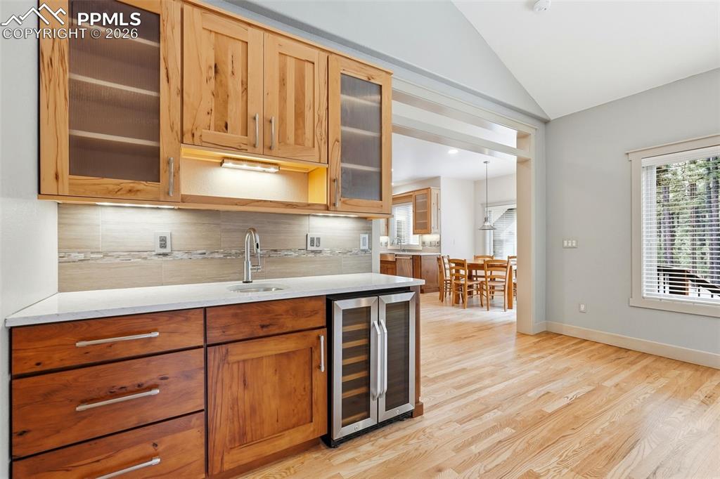 Second bar area featuring glass fronted cabinets, wine cooler, tasteful backsplash, wood flooring and vaulted ceiling