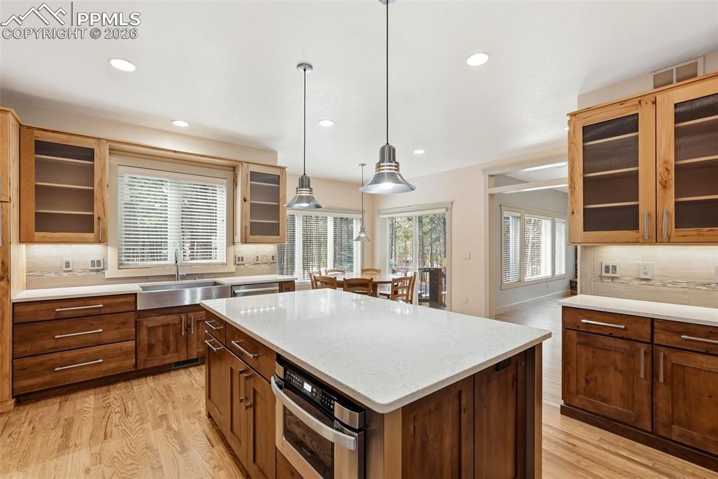 Kitchen featuring decorative backsplash, glass fronted cabinets, a center island, and hanging light fixtures