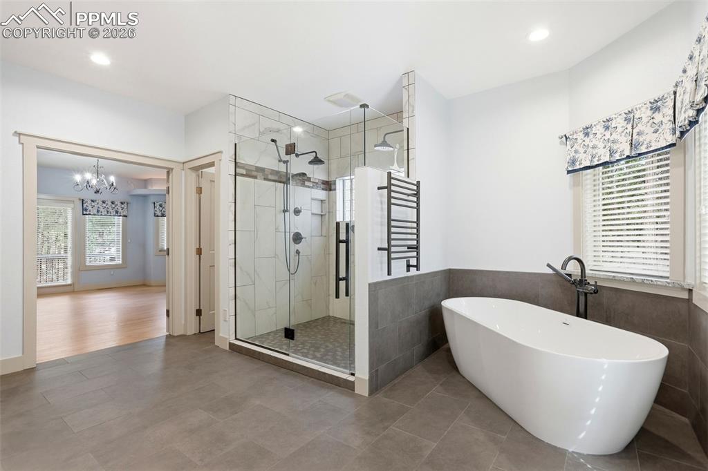 Full bathroom with a freestanding tub, a shower stall, suspended lighting, a towel warming rack, and wainscoting