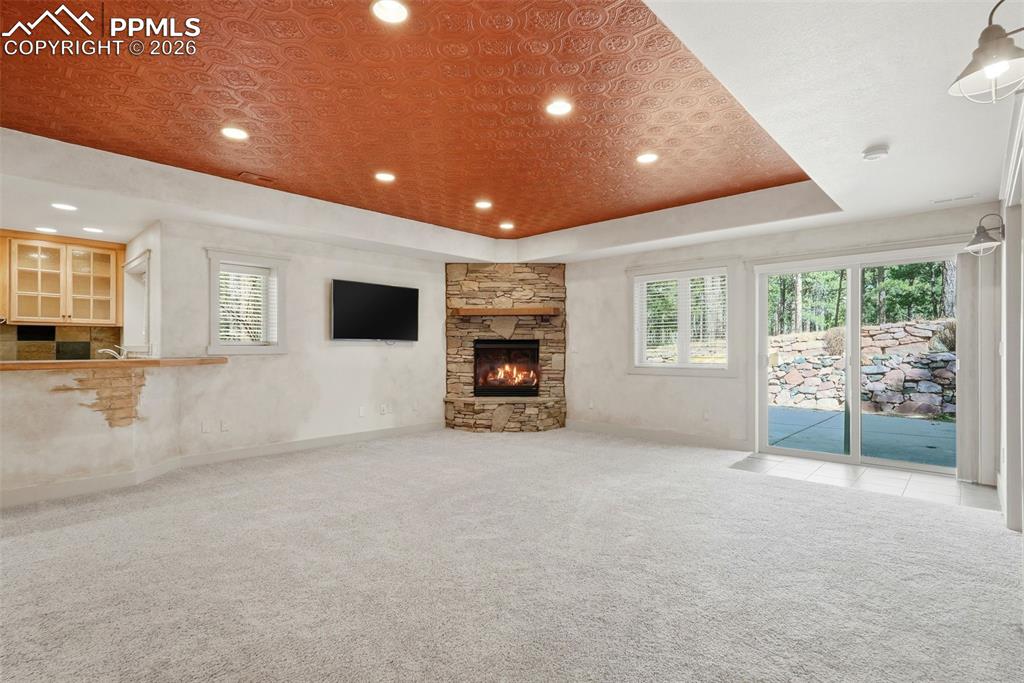 Family Room with a tray ceiling, carpet floors, and a stone fireplace