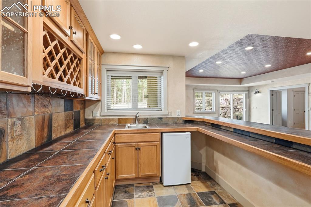 2nd Wet Bar area with stone finish flooring, glass fronted cabinets, recessed lighting, wood finish cabinets, and tasteful backsplash