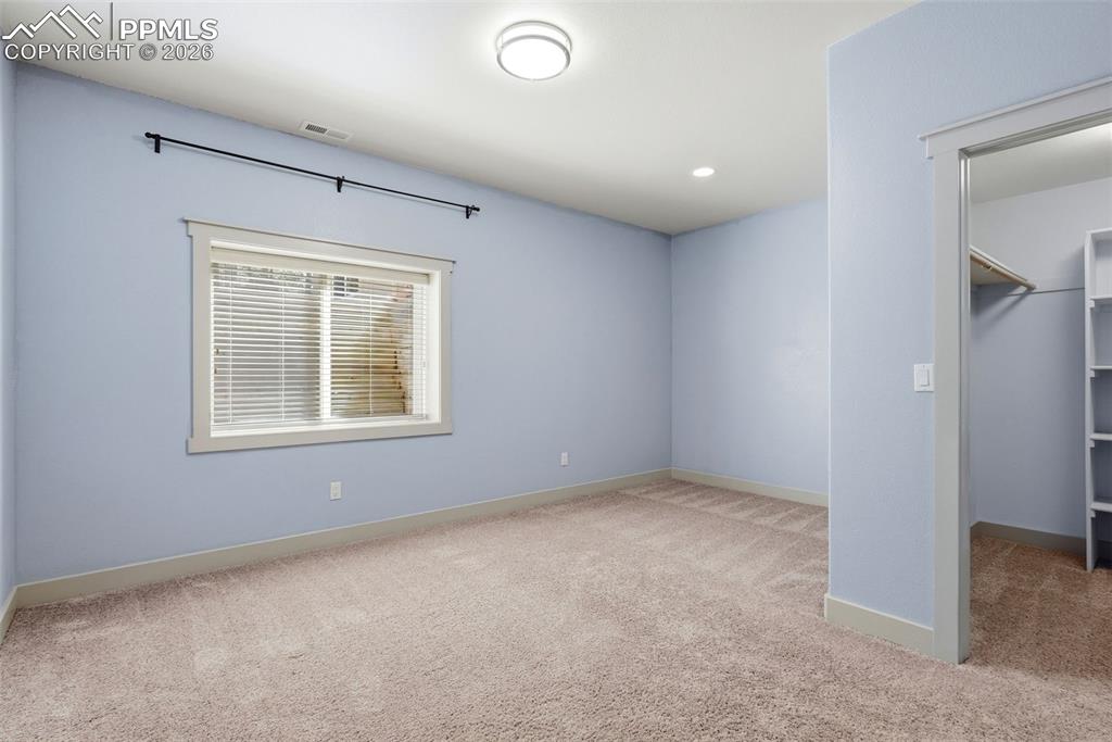 5th bedroom with light colored carpet and a walk in closet