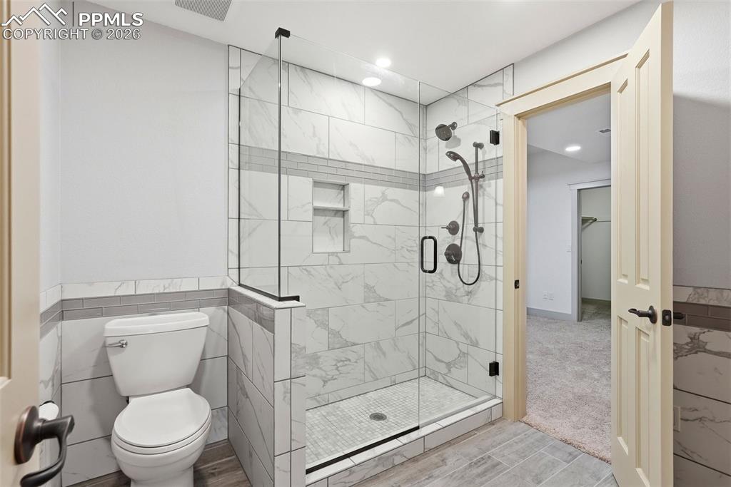 Full bath with a shower stall, tile walls, wood finish floors, recessed lighting, and a wainscoted wall