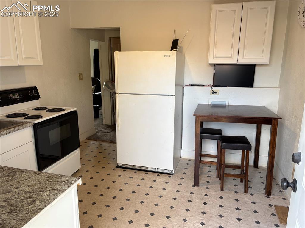 Kitchen with white cabinetry, range with electric stovetop, freestanding refrigerator, and light floors