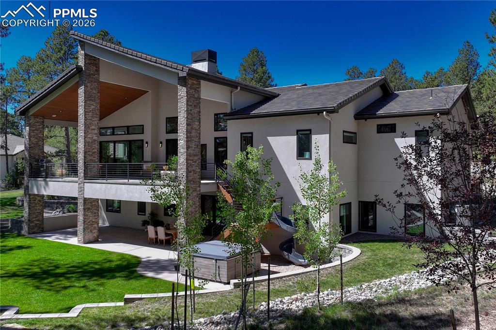 Rear view of property featuring stucco siding, a patio area, a lawn, a chimney, and a balcony